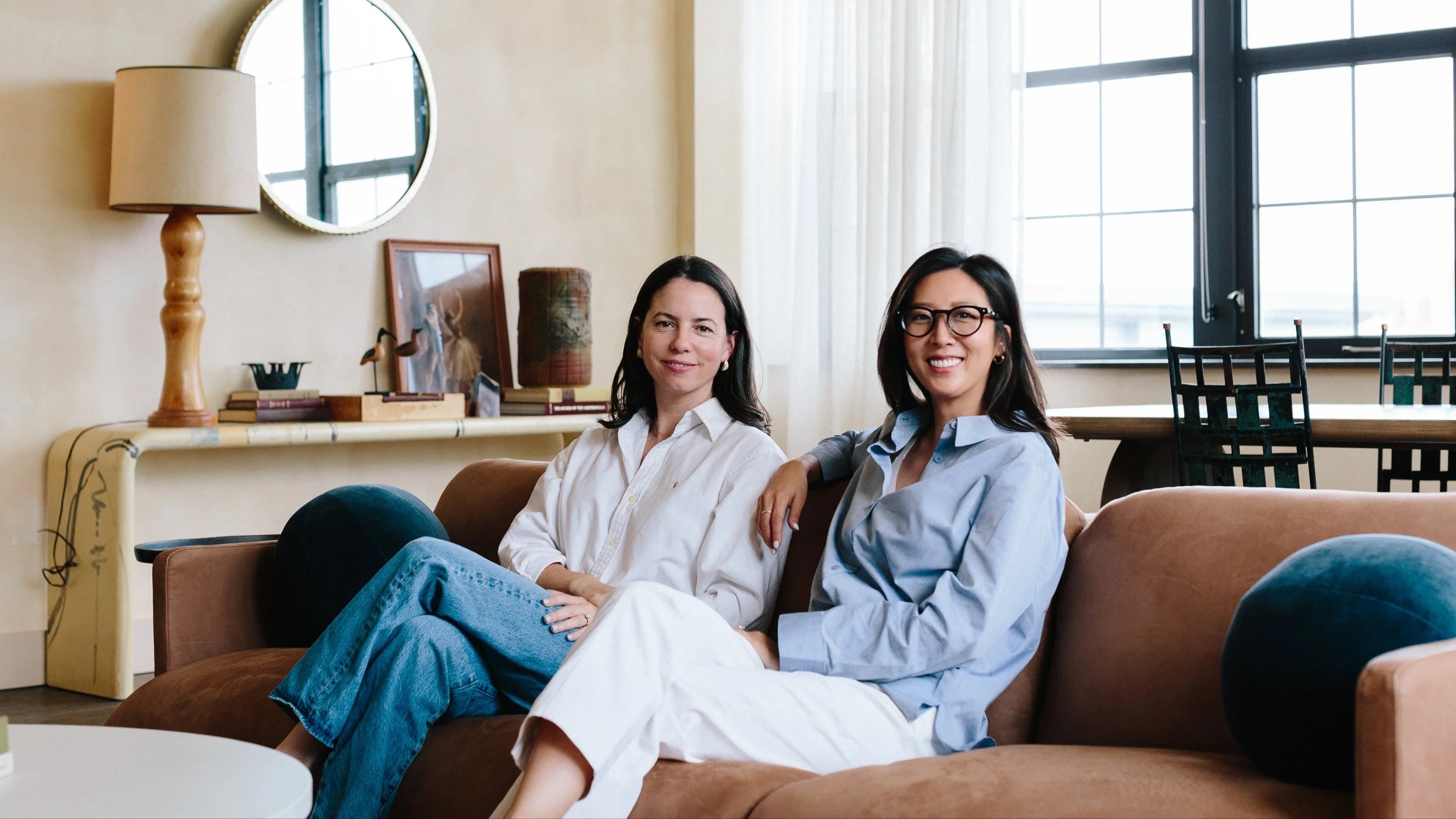 Seen Nutrition founders sitting on a couch in a living room with a lamp and mirror in the background.